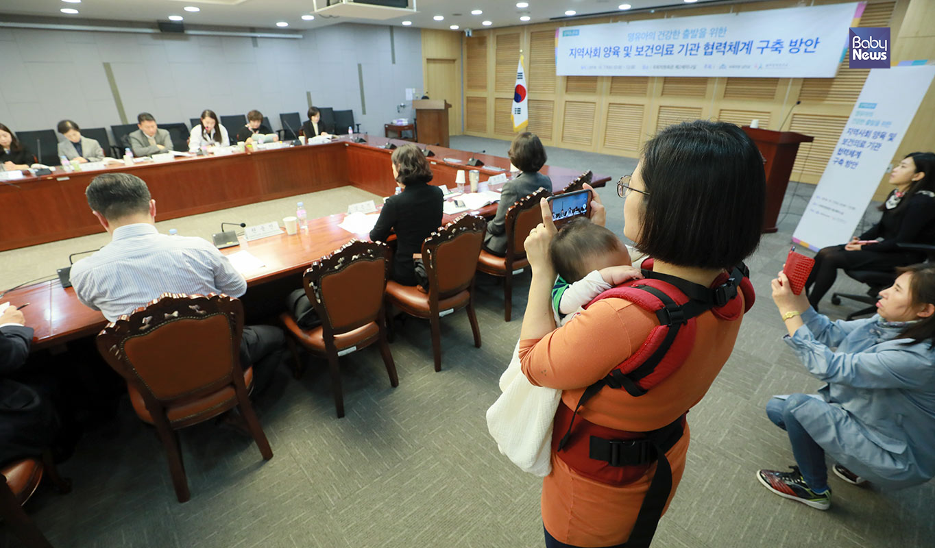 아이를 안은 한 엄마가 17일 오전 서울 국회 의원회관서 열린 영유아의 건강한 출발을 위한 지역사회 양욱 및 보건의료 기관 협력체계 구축 방안 정책 토론회에 참석해 핸드폰으로 토론을 촬영하고 있다. 최대성 기자 ⓒ베이비뉴스