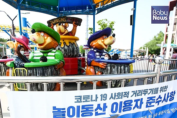 '코로나 19 사회적 거리두기' 관련 현수막이 부착돼 있는 어린이대공원 놀이기구를 탑승한 어린이들과 엄마가 마스크를 착용하고 있다. 서종민 기자 ⓒ베이비뉴스